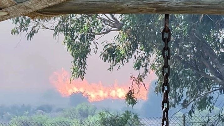 parts of a pegola in the foreground with a fire in bushland just behind a wire fence