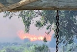 parts of a pegola in the foreground with a fire in bushland just behind a wire fence