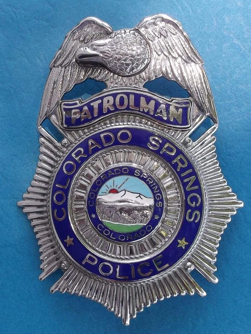 A silver police badge for the Colorado Springs area, with an American Eagle at the top.