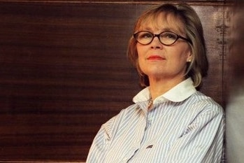 A woman in glasses and a striped shirt looks at the camera.