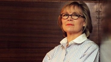 A woman in glasses and a striped shirt looks at the camera.