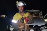 A man in a hard hat and high vis holding a dog after a rescue