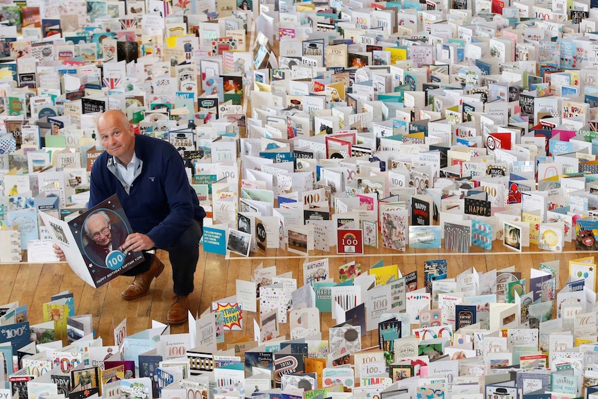 A man squats in a hall surrounded by birthday cards.