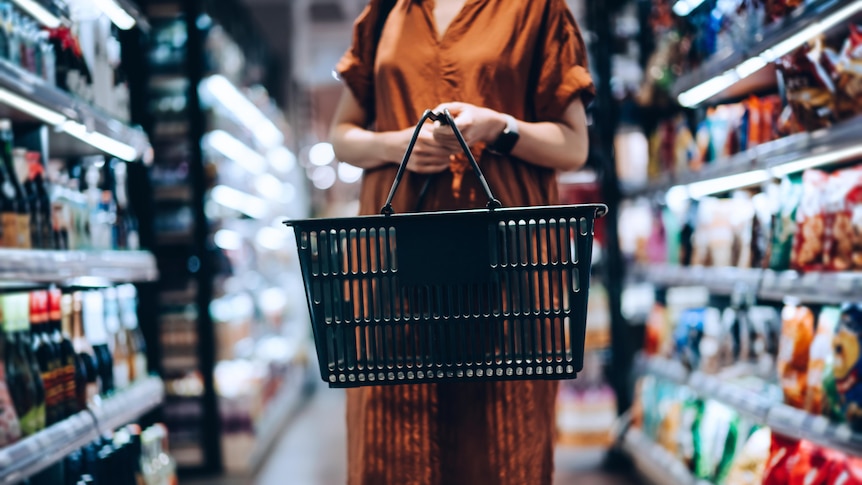 a woman standing in a supermarket holding an empty shopping basket