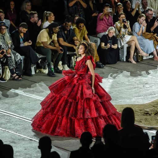 A woman wearing a beautiful red dress with ruffle upon ruffle trailing to the floor.