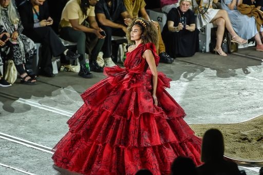 A woman wearing a beautiful red dress with ruffle upon ruffle trailing to the floor.