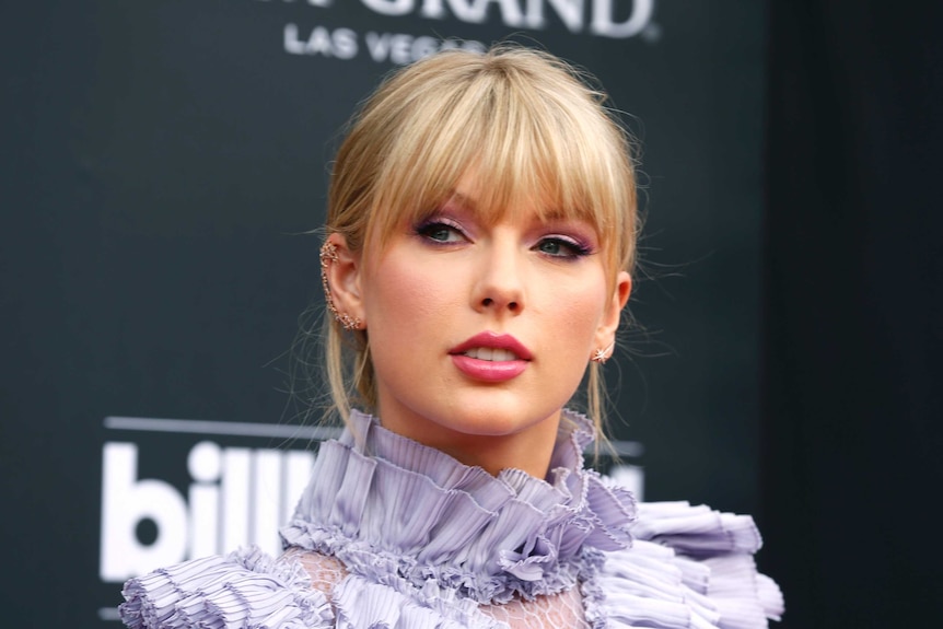 Taylor Swift, wearing a purple dress, poses for a photo.