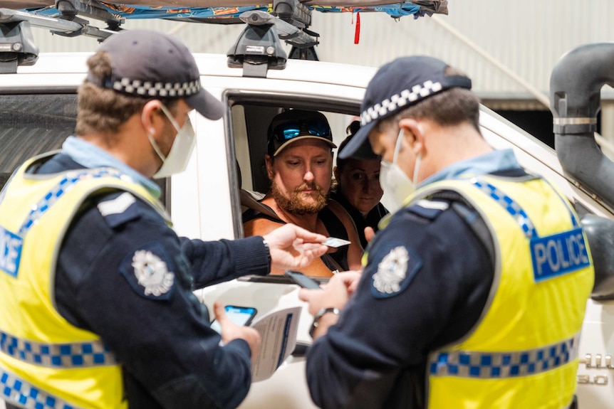 Two police officers stand next to the window of a utility checking the licence details of the driver.