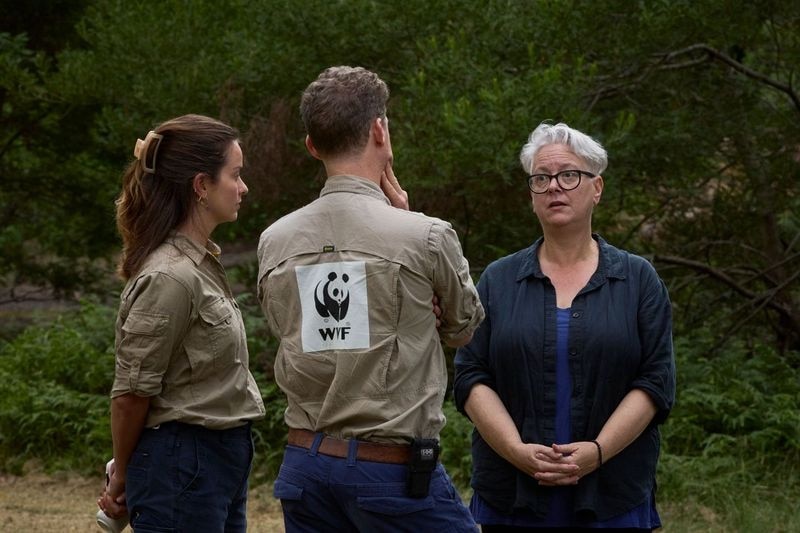 Short grey haired woman wearing dark clothing standing with zoo keepers