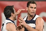 Two Geelong AFL players embrace as they celebrate a goal.