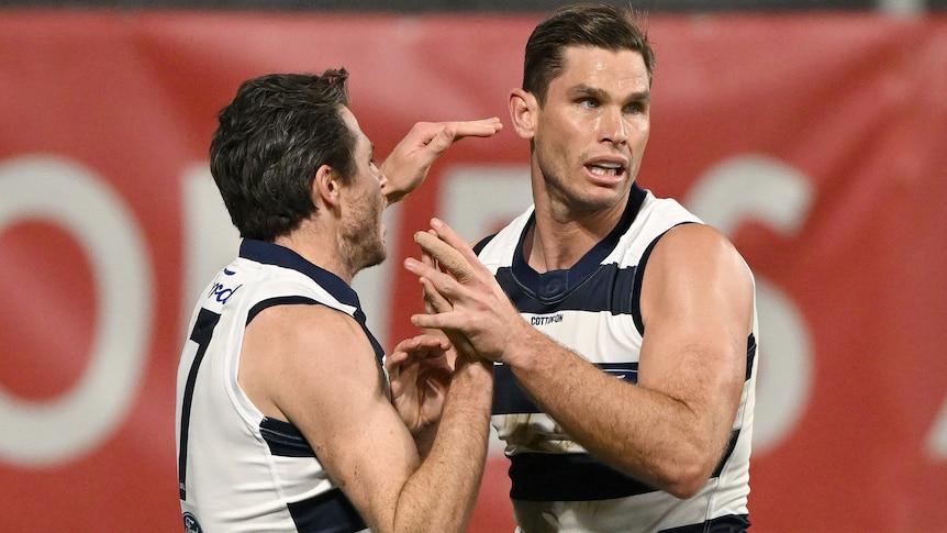Two Geelong AFL players embrace as they celebrate a goal.
