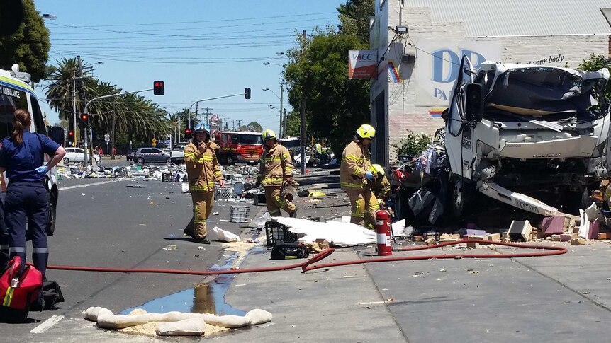 Fire crews work at the scene of the explosion, with the damaged truck in shot and debris across the road.