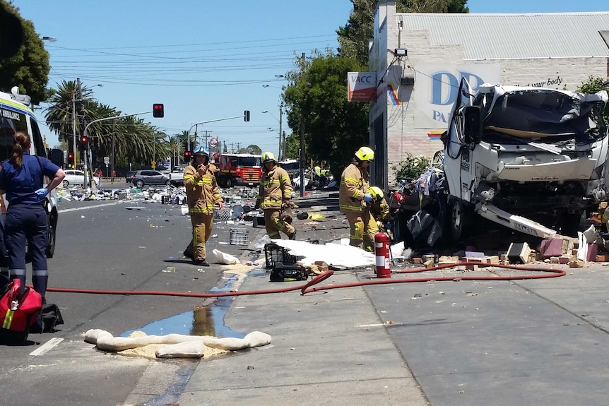 Fire crews work at the scene of the explosion, with the damaged truck in shot and debris across the road.