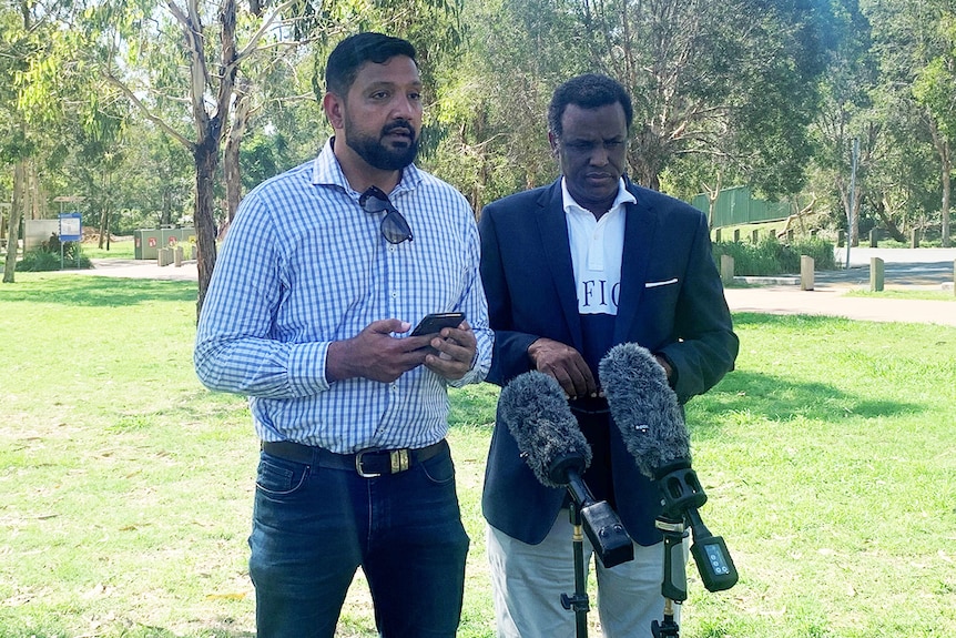 Ali Kadri, with Mohamed Abdi on his right, speaks to the media in a park in Brisbane.