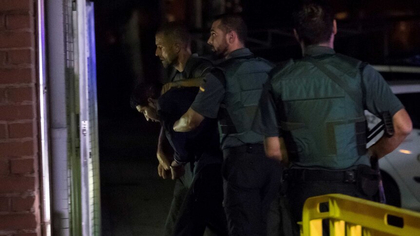 Spanish Civil Guards escort a man into a building's door.