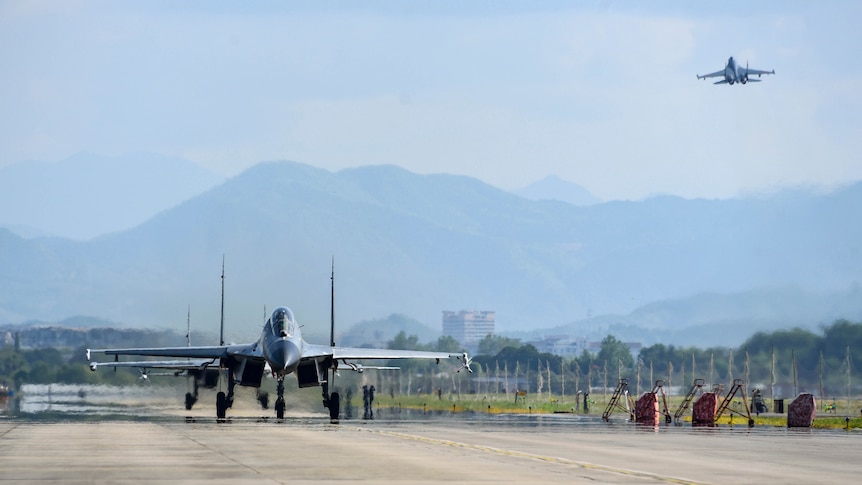 Military jet seen on tarmac as another is seen in the sky above.