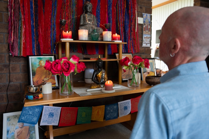 A balding man looks at a shrine with candles and flowers