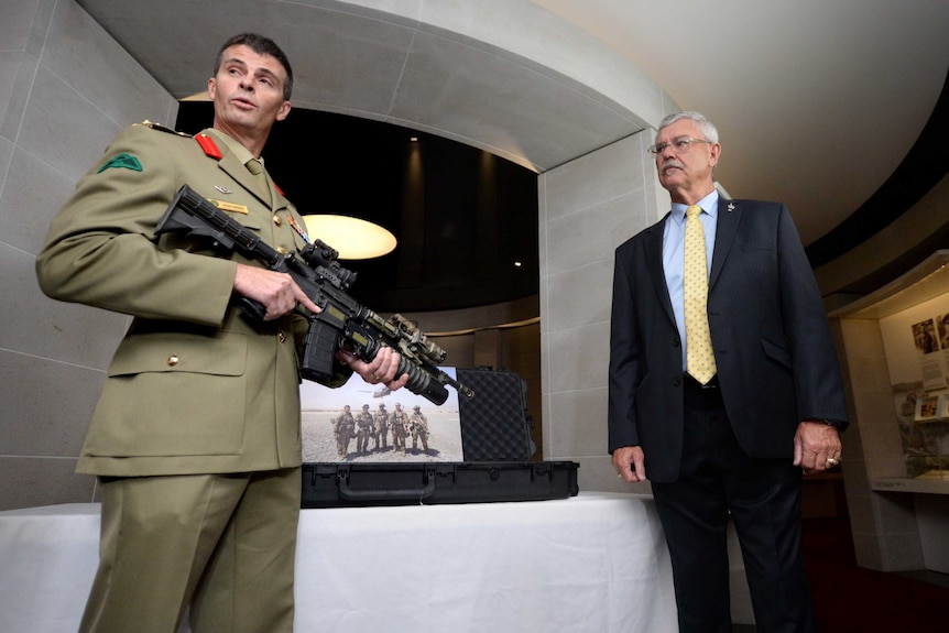 Colonel Craig Shortt holds Corporal Baird's M4 Carbine alongside Doug Baird.