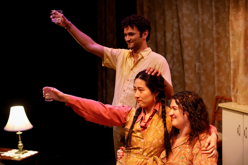 Three young people - one man and two women - in what looks like a living room, cheersing someone unseen.