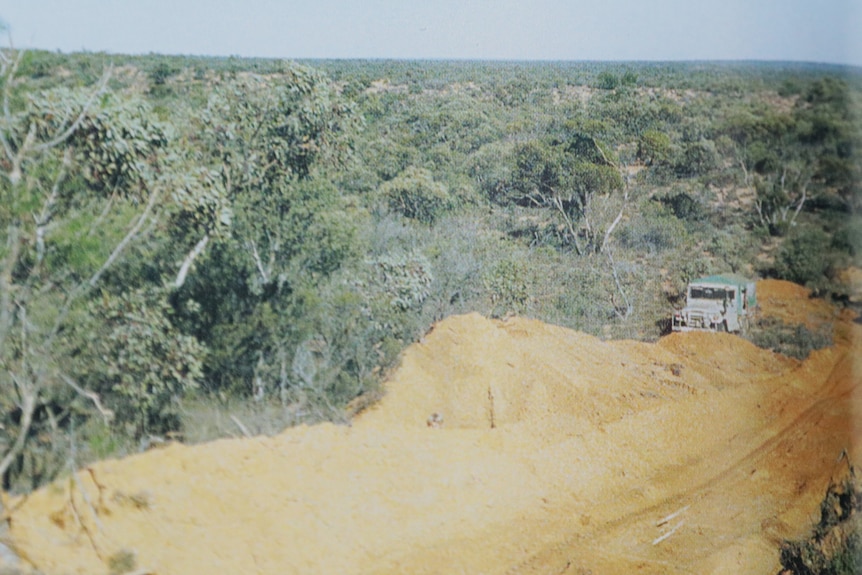 Pile of yellow sand on road with car bogged, green bush all round