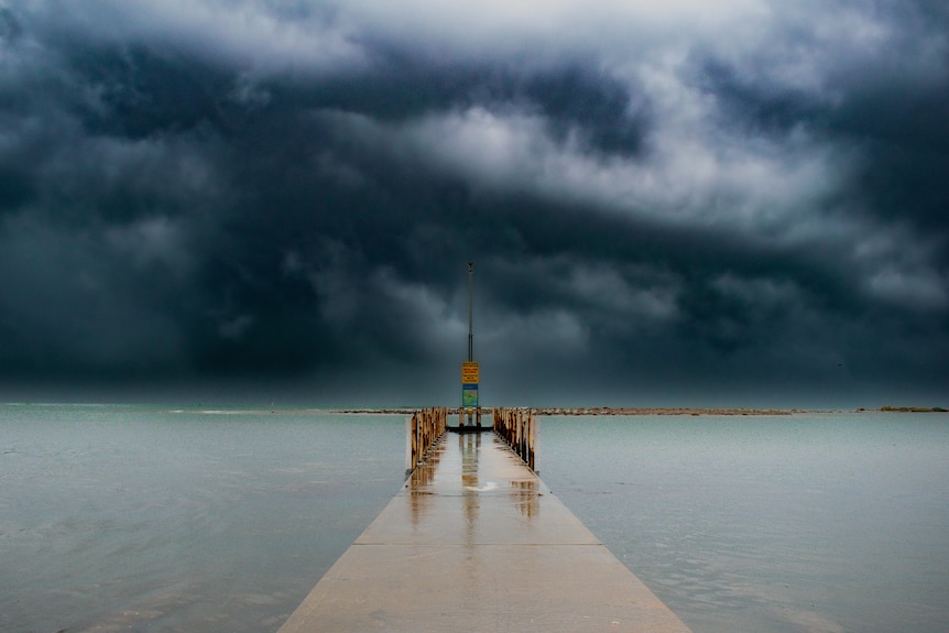 A jetty submerged with foreboding, dark clouds in the distance. 