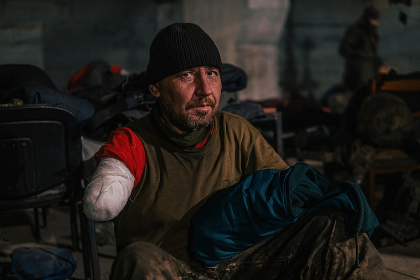 A man who has lost his arm just above his elbow sits bandaged up.