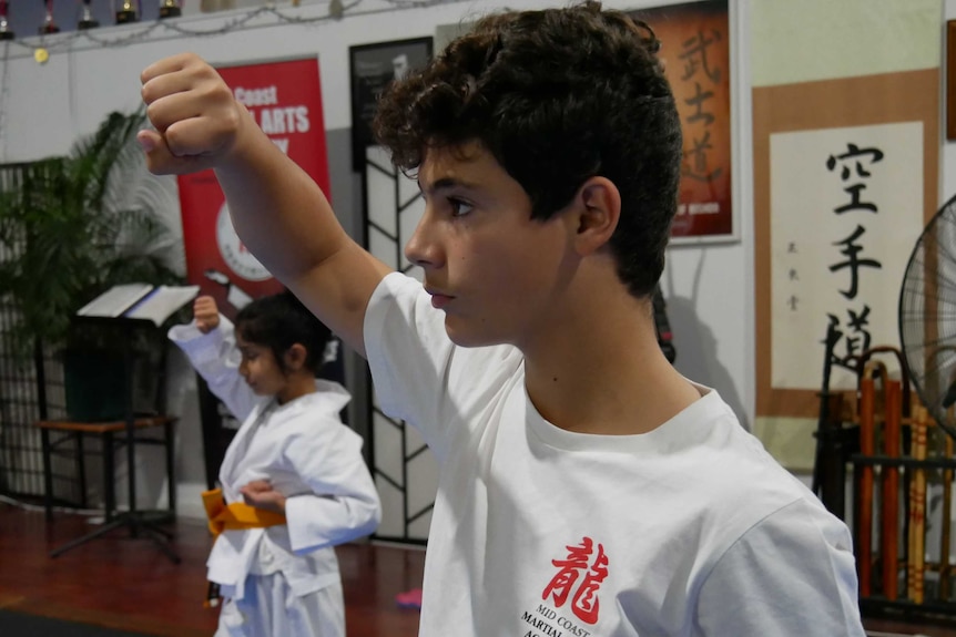 A boy holds a posture with his arm and fist up in a martial arts class.