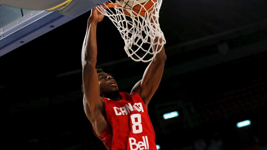Canada's Andrew Wiggins slam dunks the ball, holding the rim while looking skywards