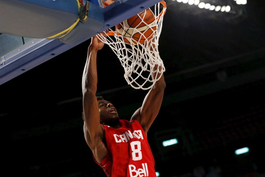 Canada's Andrew Wiggins slam dunks the ball, holding the rim while looking skywards