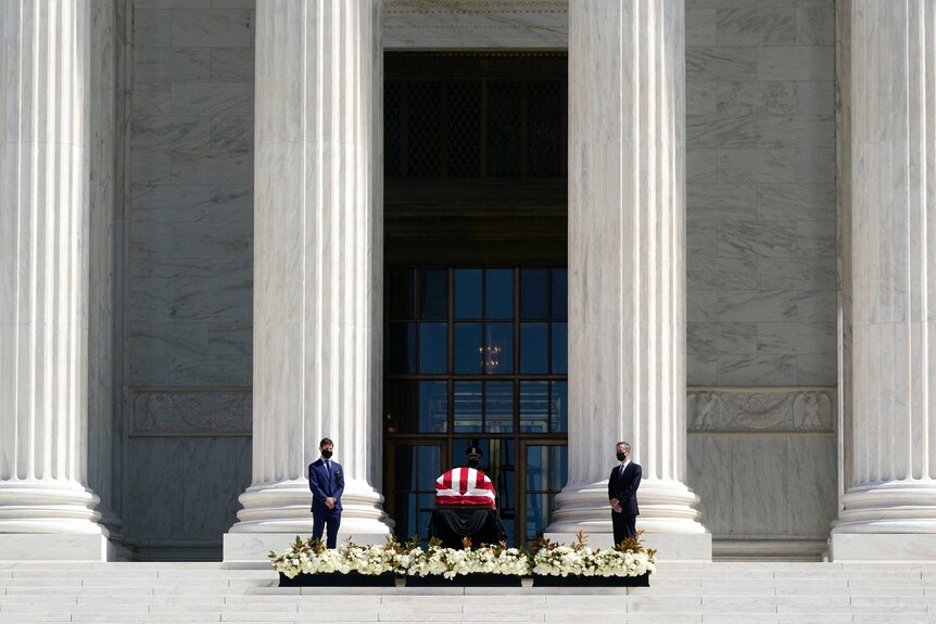 Two men in face masks standing guard over a coffin draped with an American flag