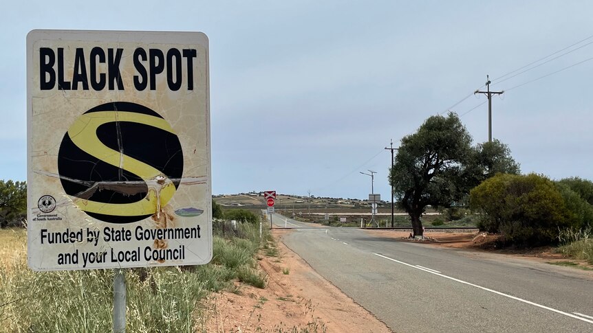 A black spot sign near a level crossing on a country road.