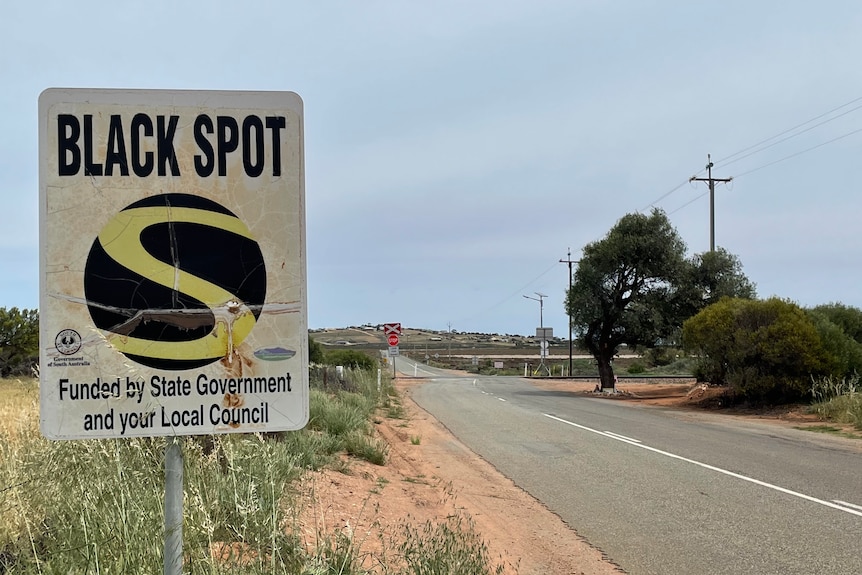 A black spot sign near a level crossing on a country road.