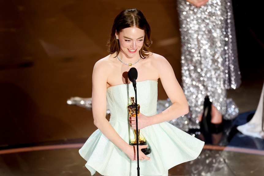 Emma clutches her Oscar on stage and smiles.
