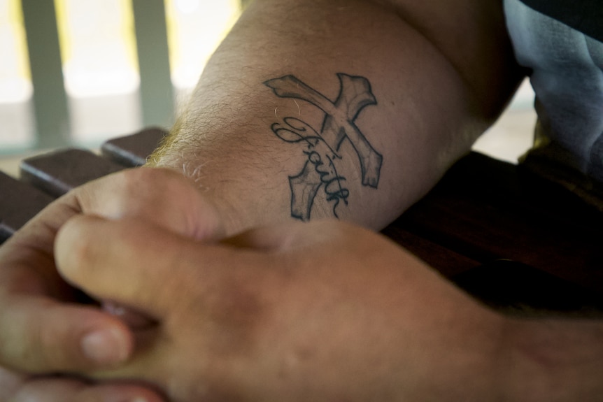 Close-up of a man's arm with a crossed tattoo and the word 