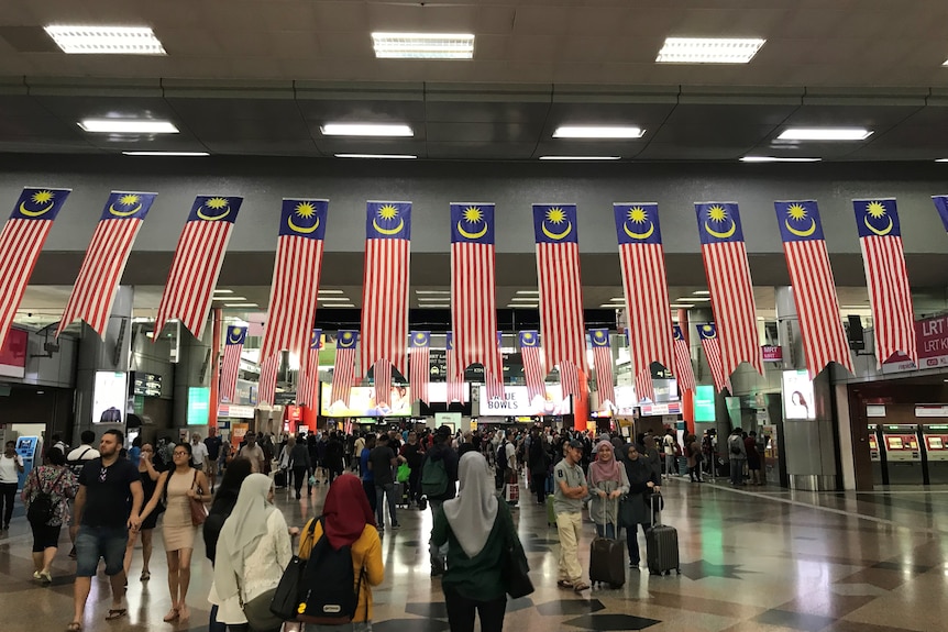 People walk under Malaysian flags at a busy train station