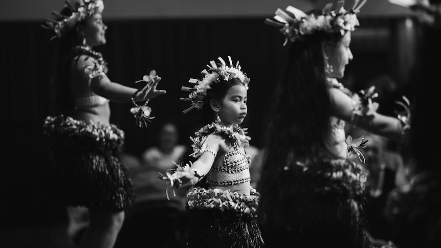 A black and white photo of children in traditional islander costume, dancing on a stage.