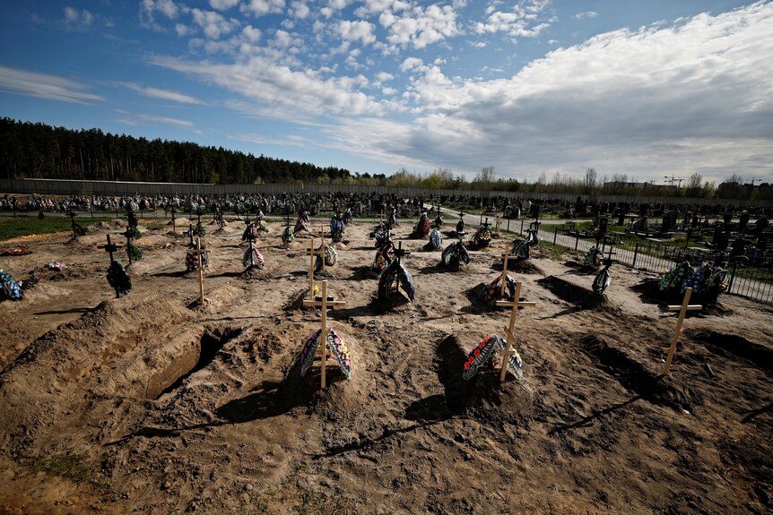 A row of graves is seen bug in the dirt with simple wooden crosses.