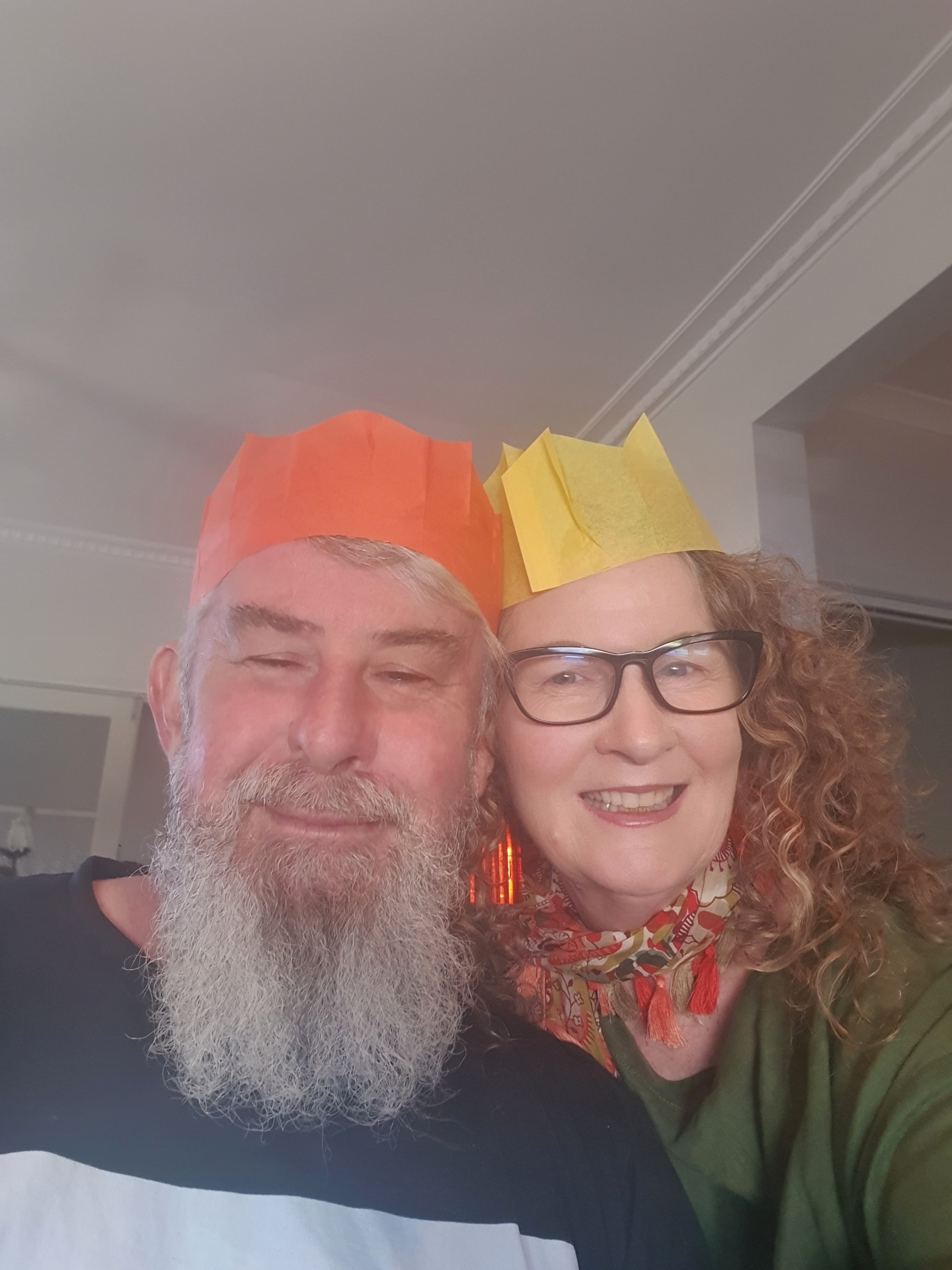 A man and woman wearing colourful Christmas paper hats smile.