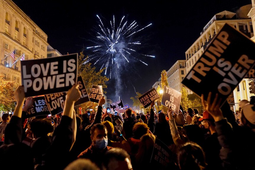 Fireworks exploding and people holding signs in a crowded street in DC