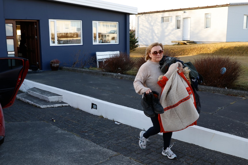 A woman is pictured carrying shoes and clothes in her arms as she walks away from a house that is painted dark blue.