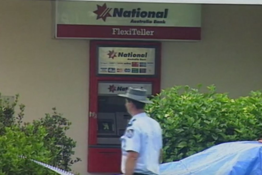 Police at scene of Browns Plains bank robbery. Red and white ATM police officer walking past. Tape around.