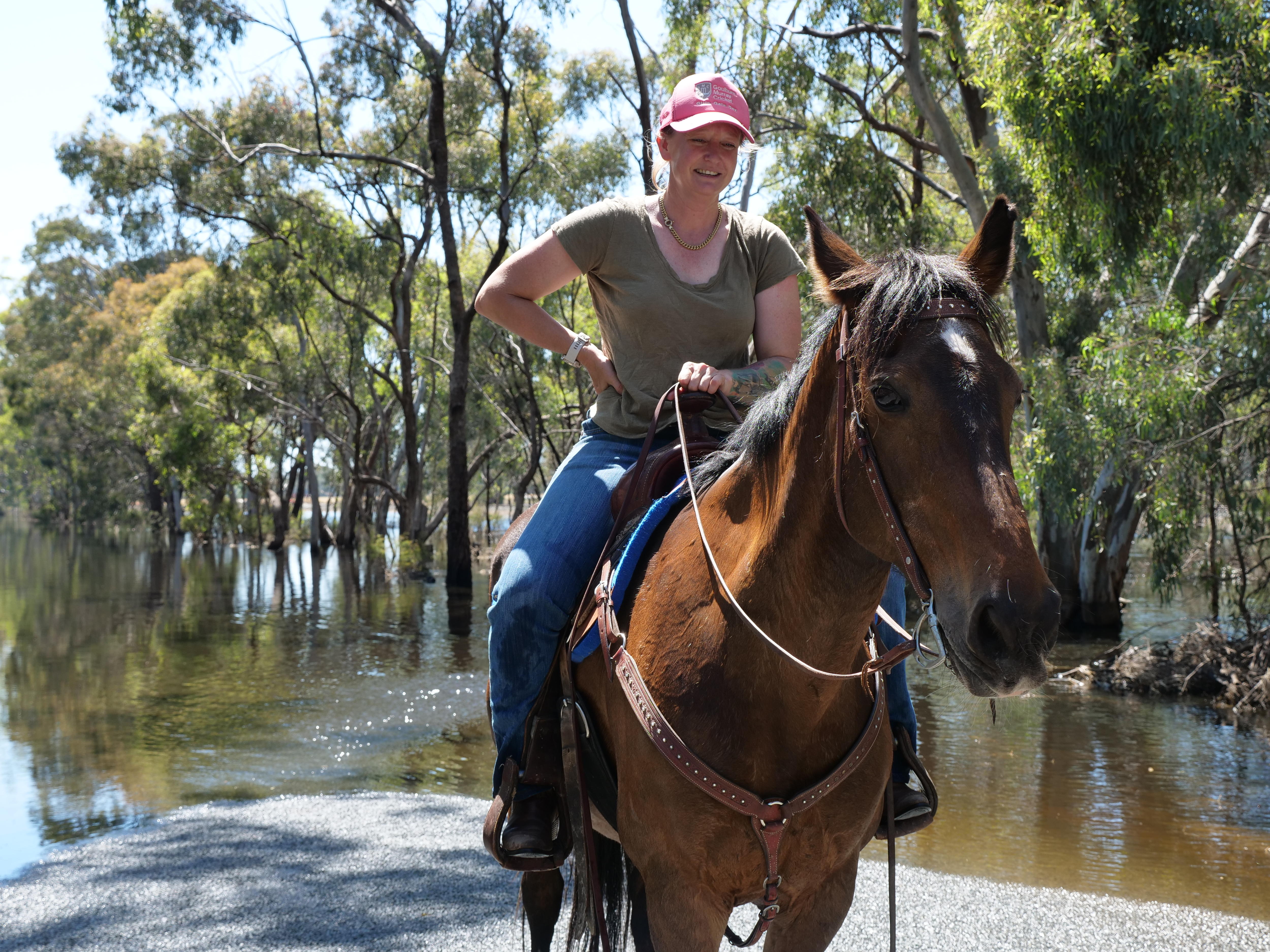 A woman riding a horse with her hand on her hip in front of a flooded road.