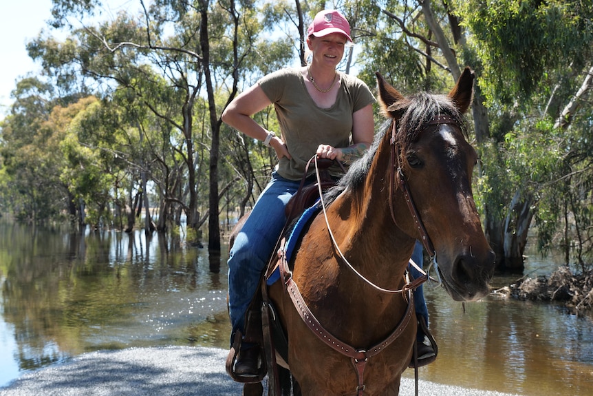 A woman riding a horse with her hand on her hip in front of a flooded road.