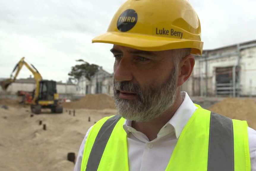 Property developer, Luke Berry, standing in the middle of a construction site with a digger in the background