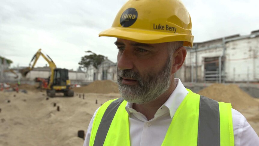 Property developer, Luke Berry, standing in the middle of a construction site with a digger in the background