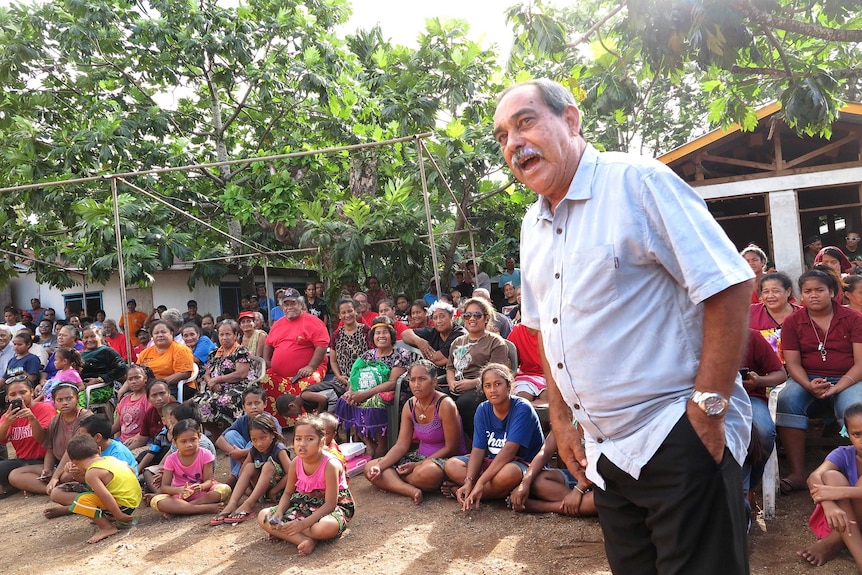 President Peter Christian stands in front of a large group of villagers in their village.
