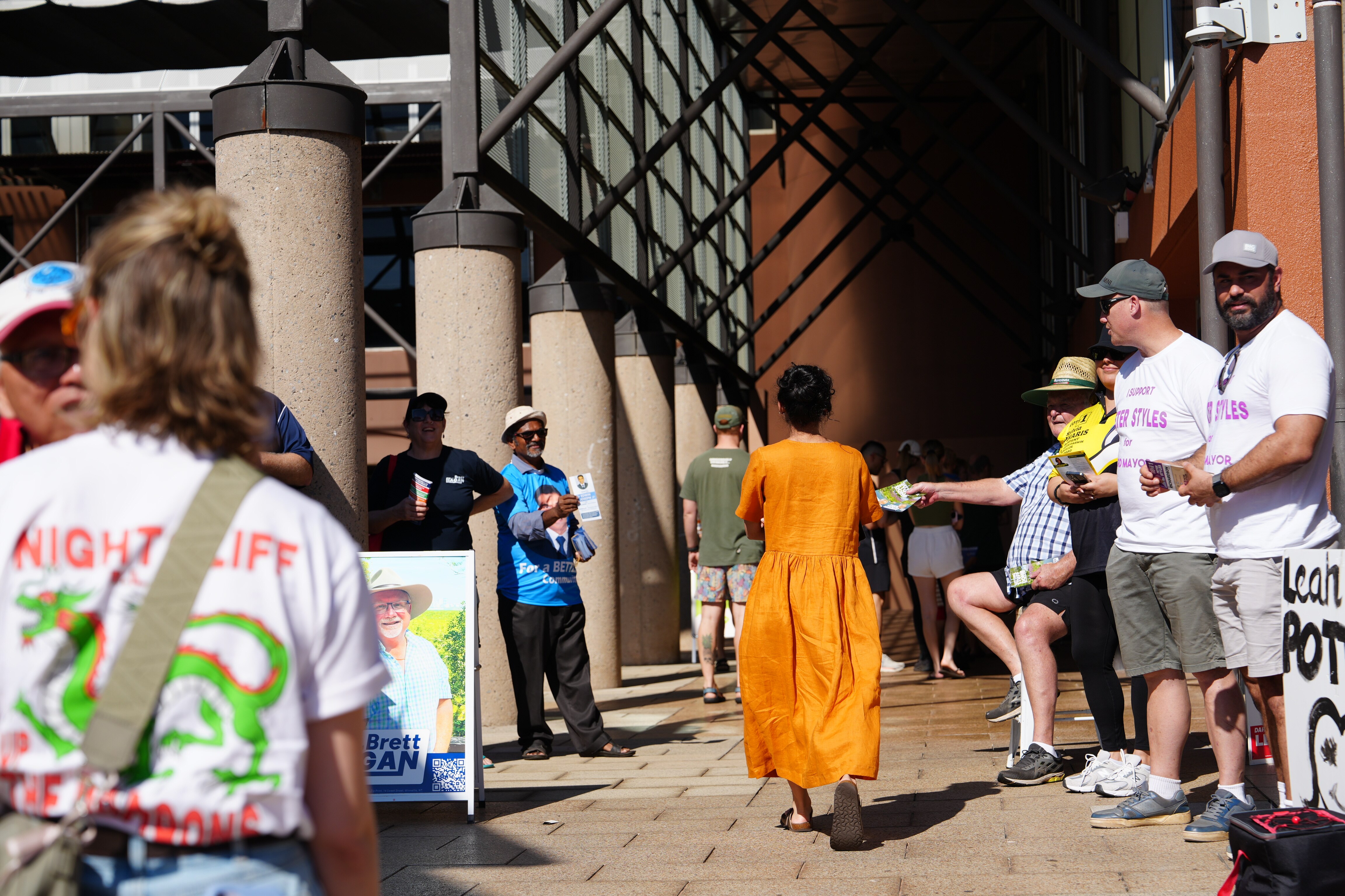 Voters walking into a polling booth, with volunteers nearby handing out how-to-vote card.