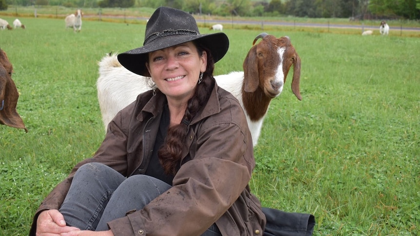Goat breeder Connie Northey sitting in a paddock surrounded by goats