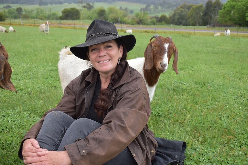 Goat breeder Connie Northey sitting in a paddock surrounded by goats