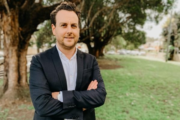 Xavier O'Halloran stands in front of trees with his arms folded.